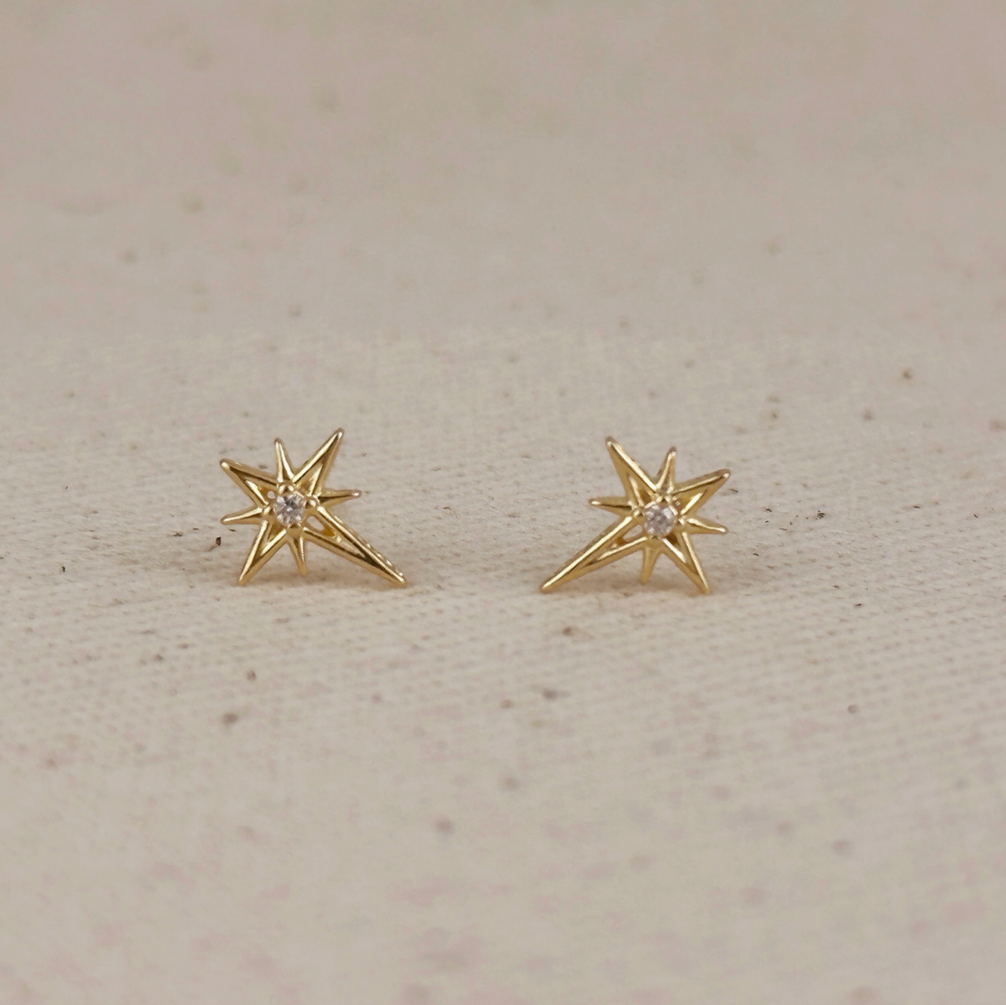 Gold star-shaped stud earrings with a central clear gemstone, gold starburst earrings featuring a sparkling center stone,Minimalist gold North Star studs with a clear crystal center, stud earrings, 18k gold earrings, water resistant earrings, karadise boutique star earrings, McKinneu Texas Star Earrings
